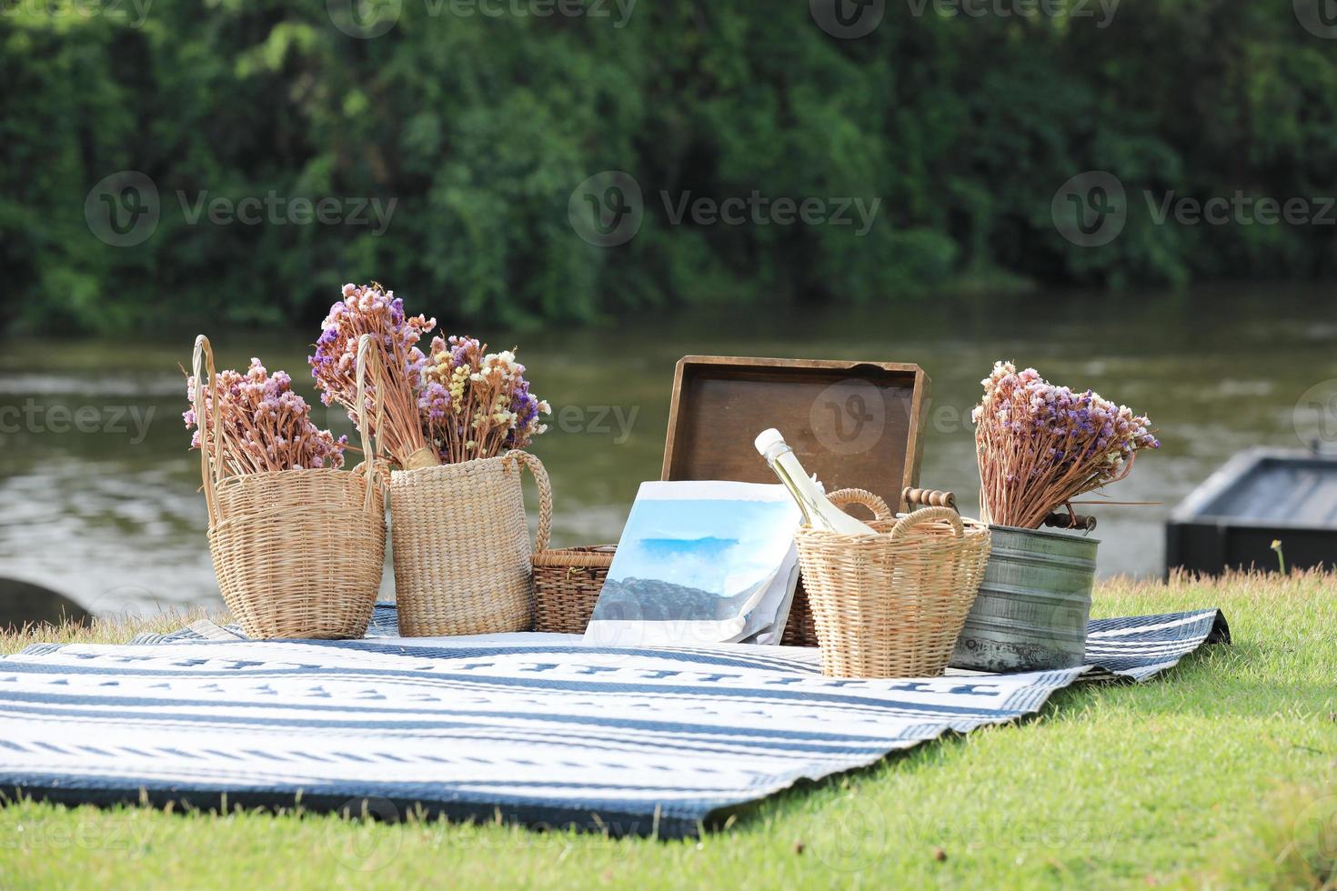 Book and flowers baskets on blue mat with river and forest in background. Vacation concept. photo