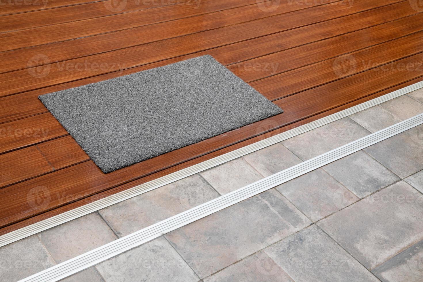 Dark gray doormat on wooden floor with steps to tiled floor photo