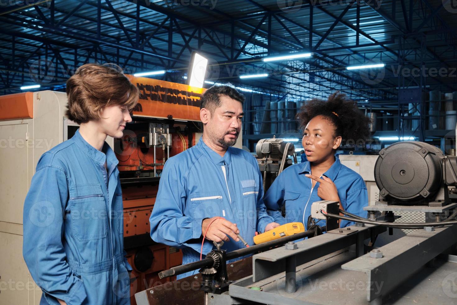 Multiracial professional industry engineer teams in safety uniforms work by inspecting machines' voltage current, checking, and maintaining at manufacture factory, electric system service occupations. photo