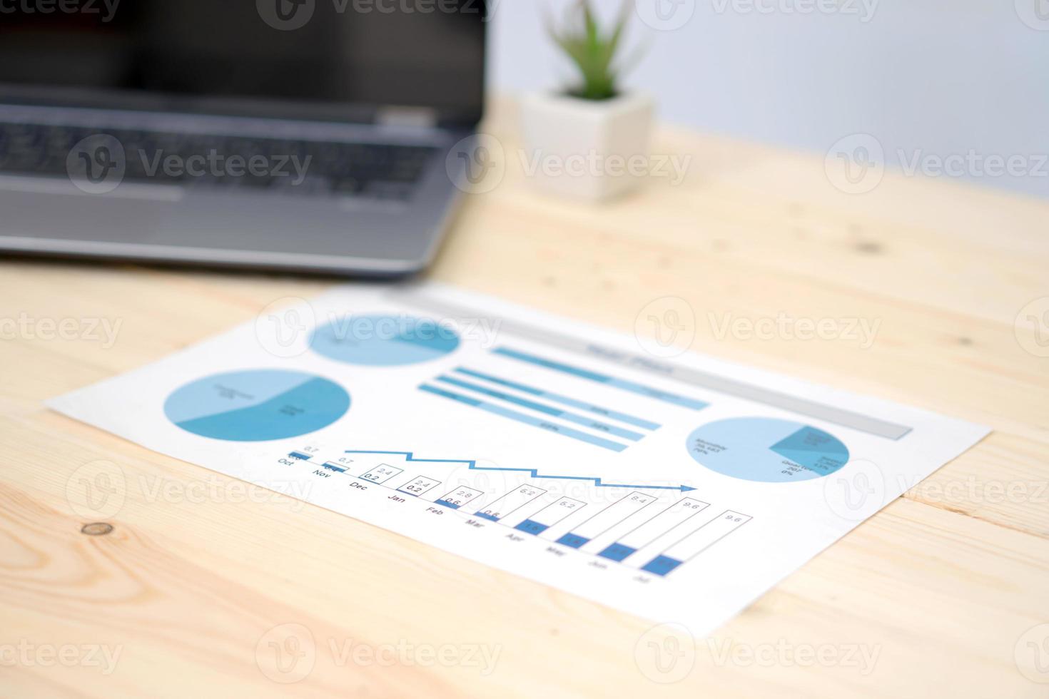 laptop and financial graph on white paper on working table photo