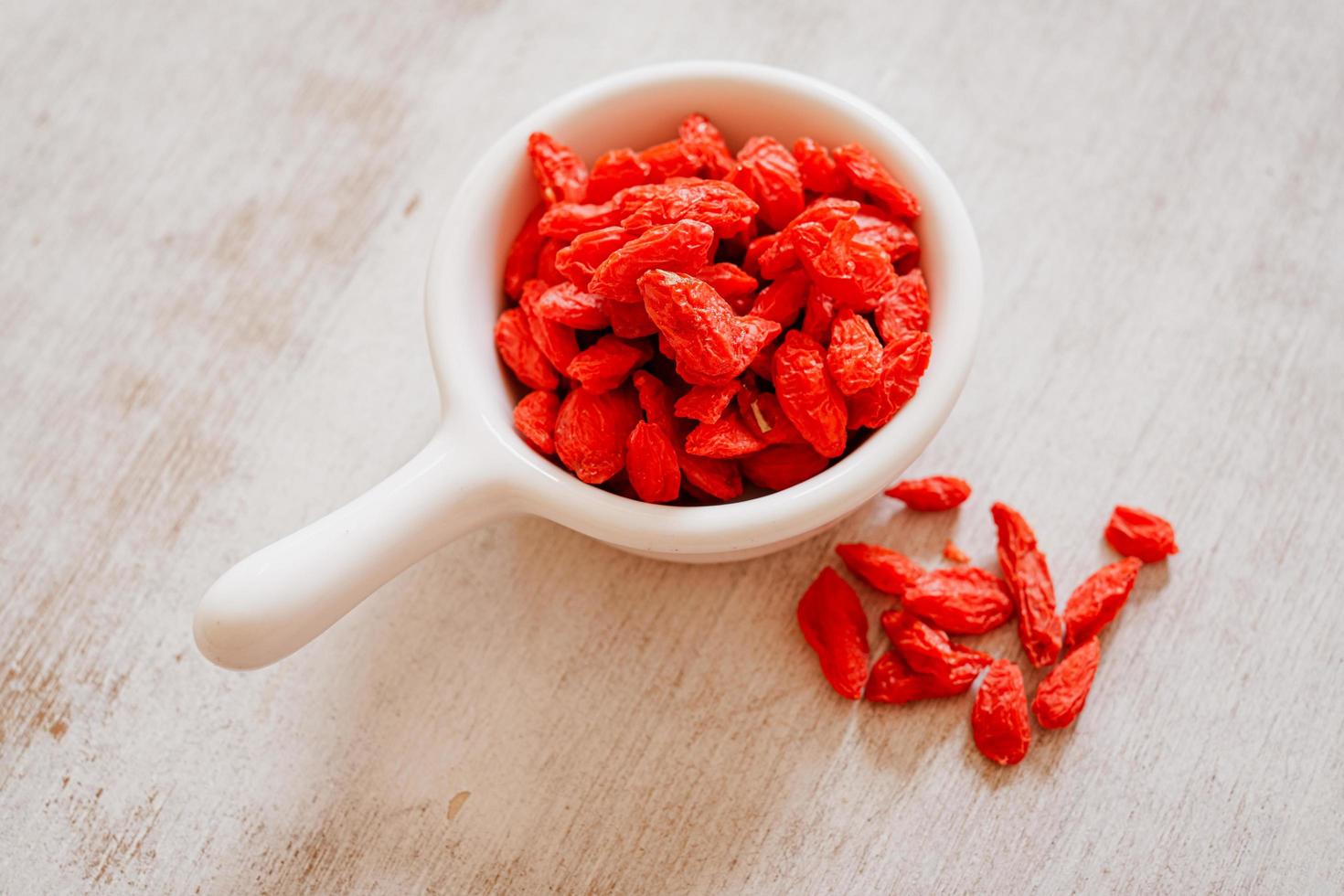 Dried Chinese wolfberries or Goji berry chinese herb or Matrimony vine in the white ceramic bowl isolated on wooden background. Top view. Selected focus. photo
