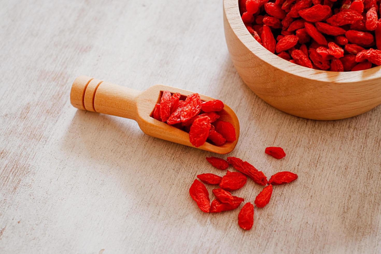 Dried Chinese wolfberries or Goji berry chinese herb or Matrimony vine in the woodden scoop on wooden bowl isolated on wooden background.  Selected focus. photo