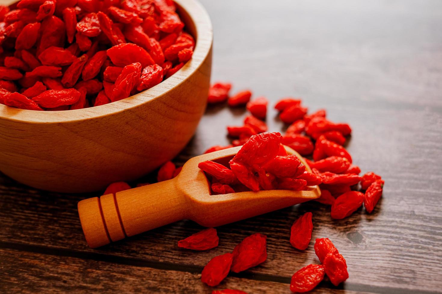 Dried Chinese wolfberries or Goji berry chinese herb or Matrimony vine in the woodden scoop on wooden bowl isolated on wooden background.  Selected focus. photo