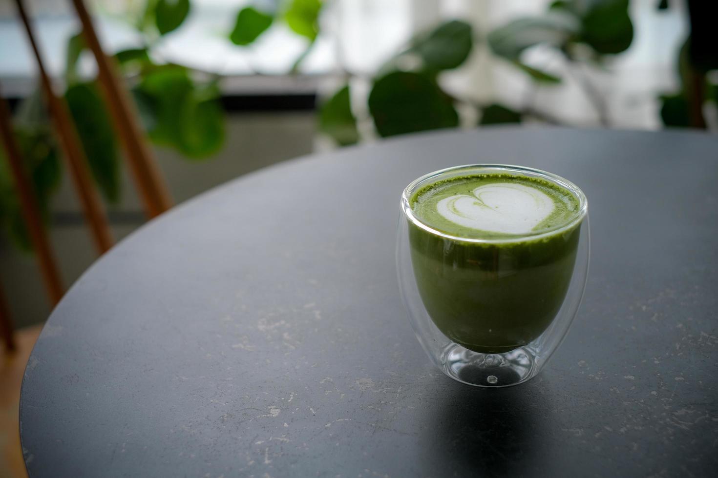 Colse up hot matcha green tea latte art in double walled glass on table in the cafe. photo