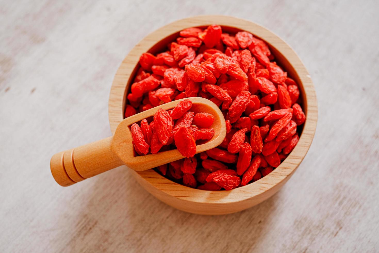 Dried Chinese wolfberries or Goji berry chinese herb or Matrimony vine in the woodden scoop on wooden bowl isolated on wooden background.  Selected focus. photo