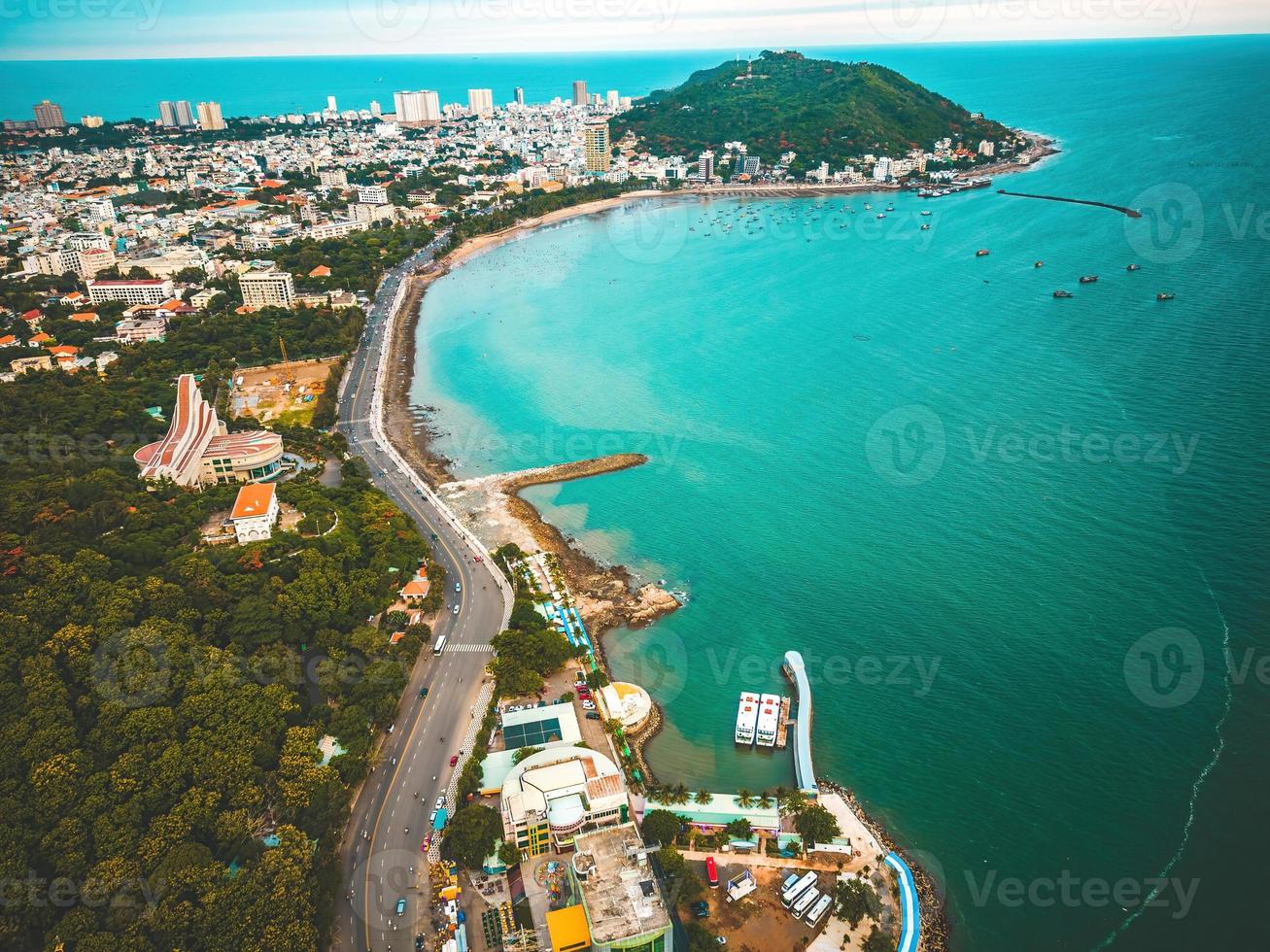 Vung Tau city aerial view with beautiful sunset and so many boats. Panoramic coastal Vung Tau view from above, with waves, coastline, streets, coconut trees and Tao Phung mountain in Vietnam. photo