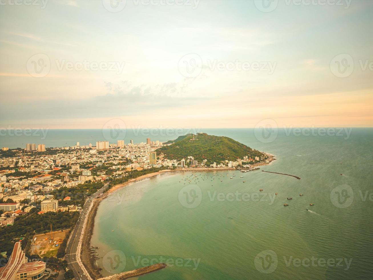 Vung Tau city aerial view with beautiful sunset and so many boats. Panoramic coastal Vung Tau view from above, with waves, coastline, streets, coconut trees and Tao Phung mountain in Vietnam. photo