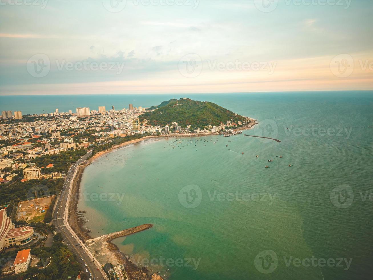 Vung Tau city aerial view with beautiful sunset and so many boats. Panoramic coastal Vung Tau view from above, with waves, coastline, streets, coconut trees and Tao Phung mountain in Vietnam. photo