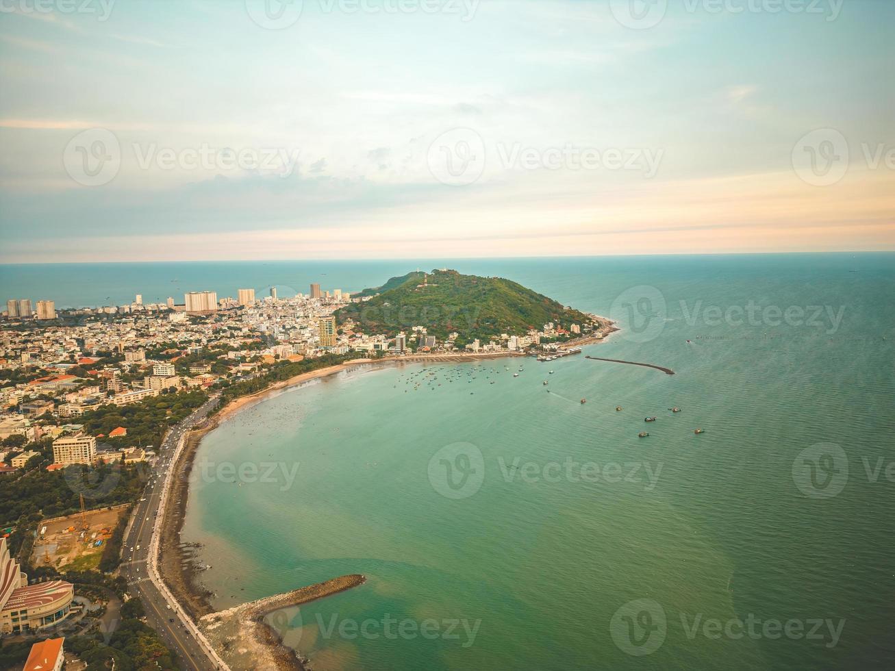 Vung Tau city aerial view with beautiful sunset and so many boats. Panoramic coastal Vung Tau view from above, with waves, coastline, streets, coconut trees and Tao Phung mountain in Vietnam. photo