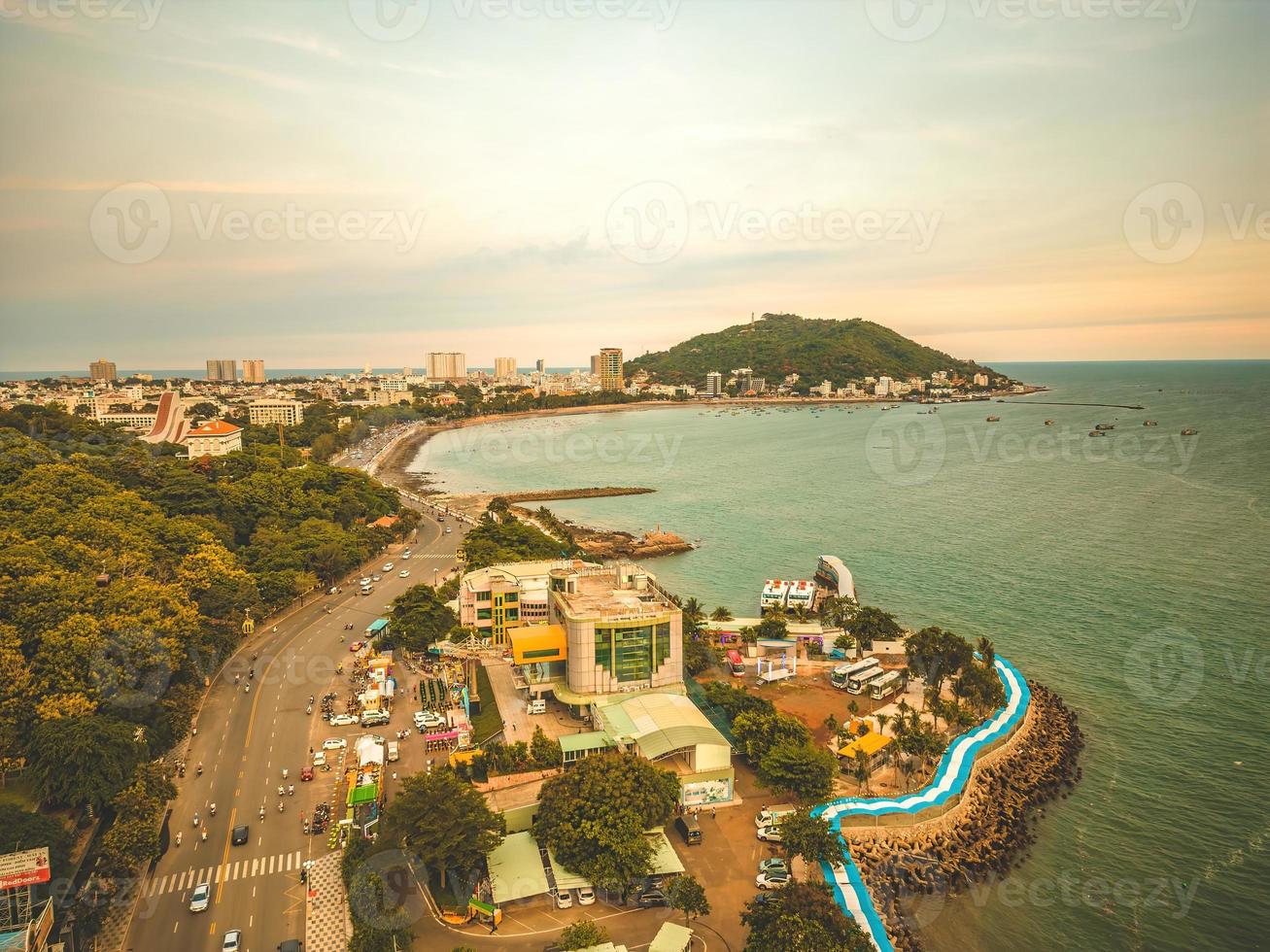 Vung Tau city aerial view with beautiful sunset and so many boats. Panoramic coastal Vung Tau view from above, with waves, coastline, streets, coconut trees and Tao Phung mountain in Vietnam. photo
