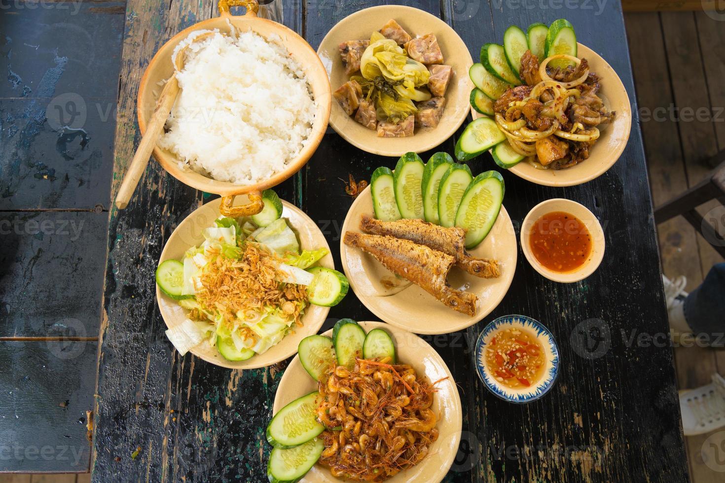cocina casera de la familia vietnam preparada para cuatro personas arroz cocido, sopa de verduras y pescado frito, cebollas fritas con pollo, rodaja de pepino, comida tradicional vietnamita en el campo. foto