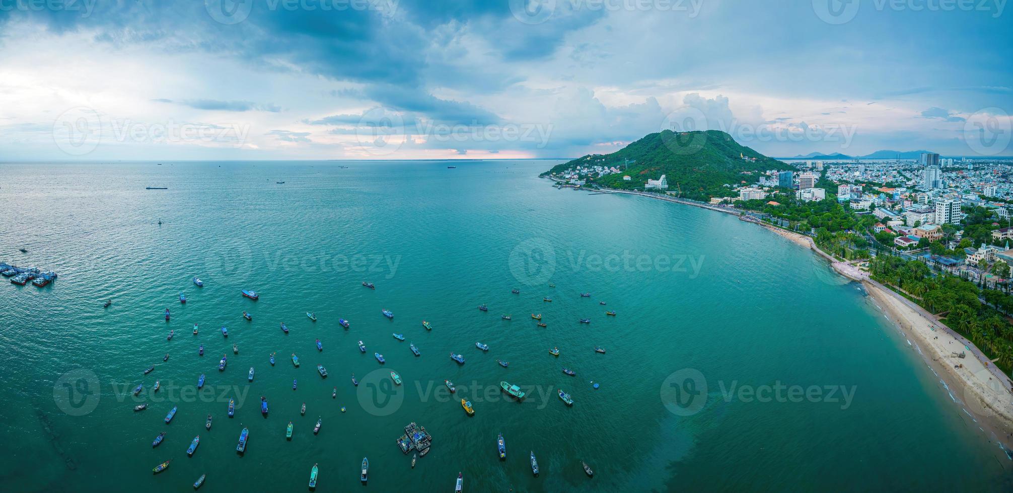 Vung Tau city aerial view with beautiful sunset and so many boats. Panoramic coastal Vung Tau view from above, with waves, coastline, streets, coconut trees and Tao Phung mountain in Vietnam. photo