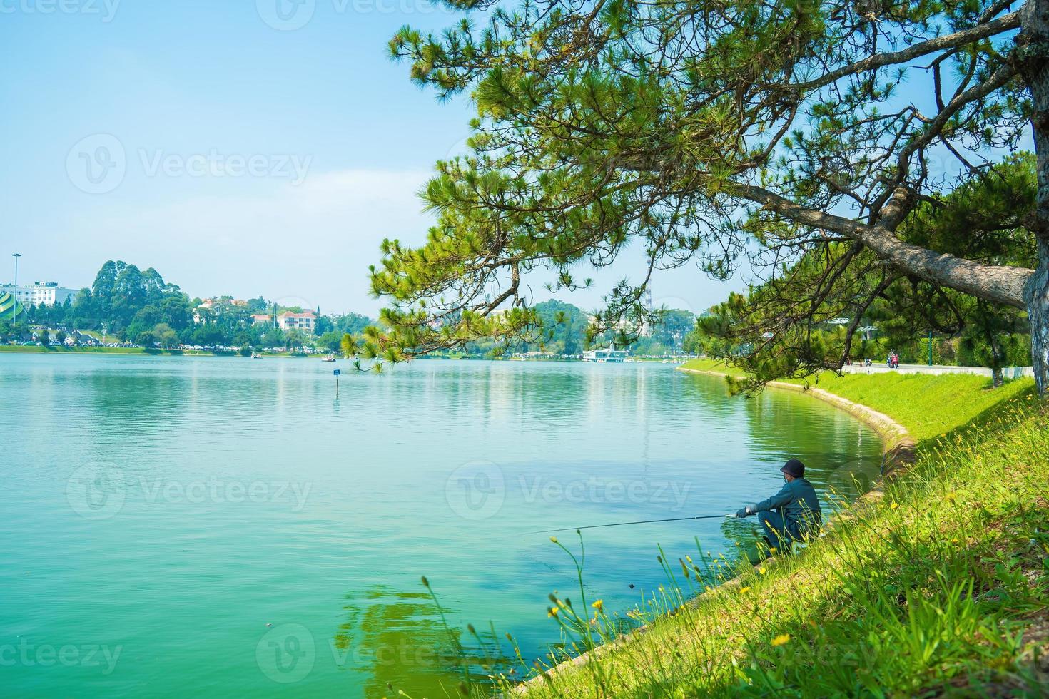 Focus young fisherman wearing medical mask using rod front of Xuan Huong Lake, in center Da Lat City, Lam Dong Province, Vietnam. photo