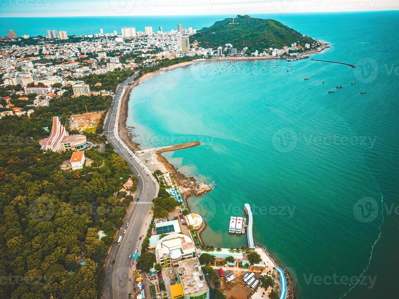 Vung Tau city aerial view with beautiful sunset and so many boats. Panoramic coastal Vung Tau view from above, with waves, coastline, streets, coconut trees and Tao Phung mountain in Vietnam. photo