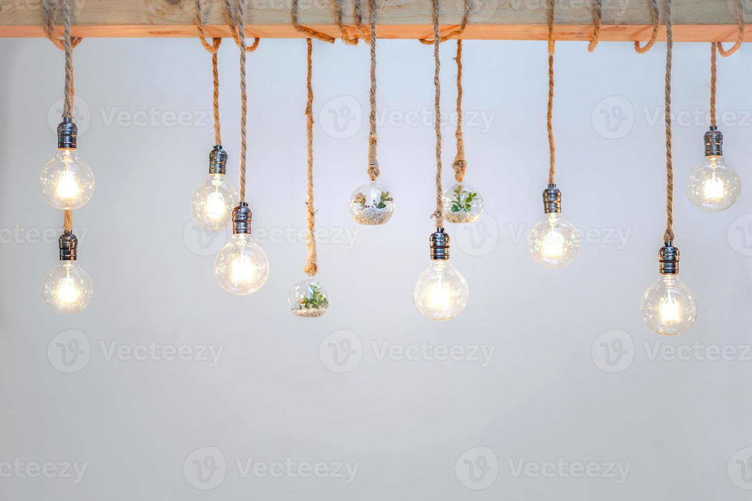 Decorated cozy lamps stick in the rope and little tiny tree with small white rock inside the ball glass hang on to big wood log in front of white background. photo