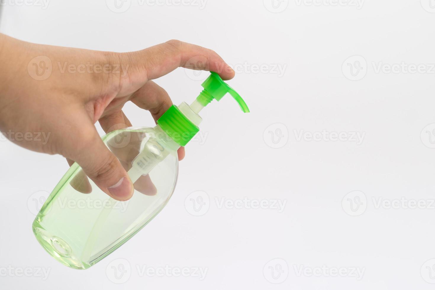 Asian mand hand holds a gel alcohol pump bottle and ready to pushes on it. It's an isolated object on the white clear screen in studio light. photo