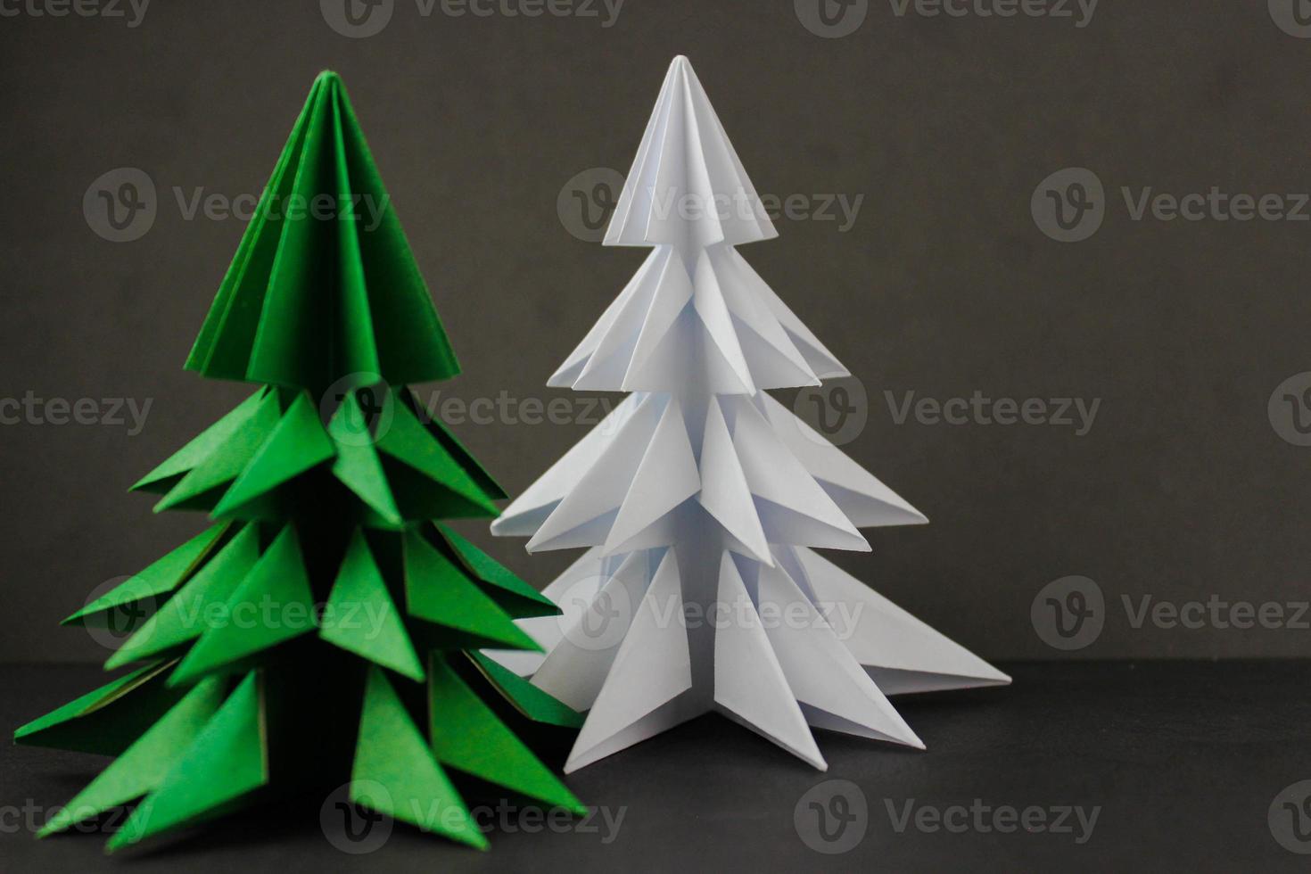 Two origami green and white christmas tree on black background. Focus on a white tree photo