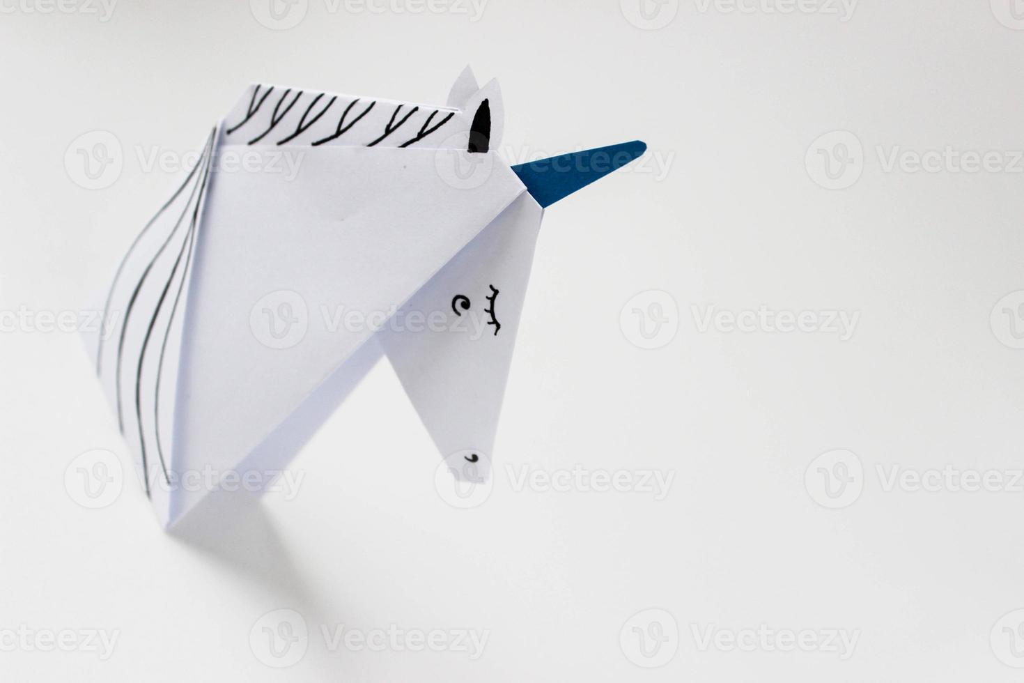 White unicorn made in the origami technique on the left side of the photo on a white background. With place for your text.