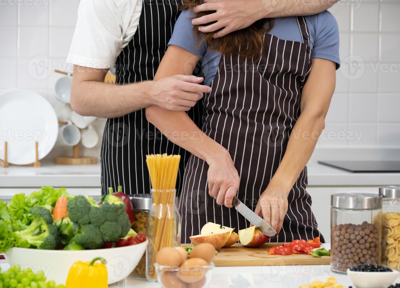 Young couple cutting apple fruit in the kitchen, girl hugging her guy. Healthy Dieting Food Concept. photo
