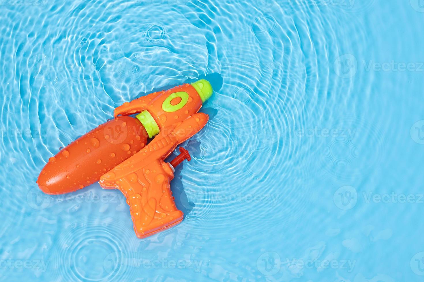 Water gun toy on blue water surface with rippled waves. Fun, leisure summertime background. Copy space photo