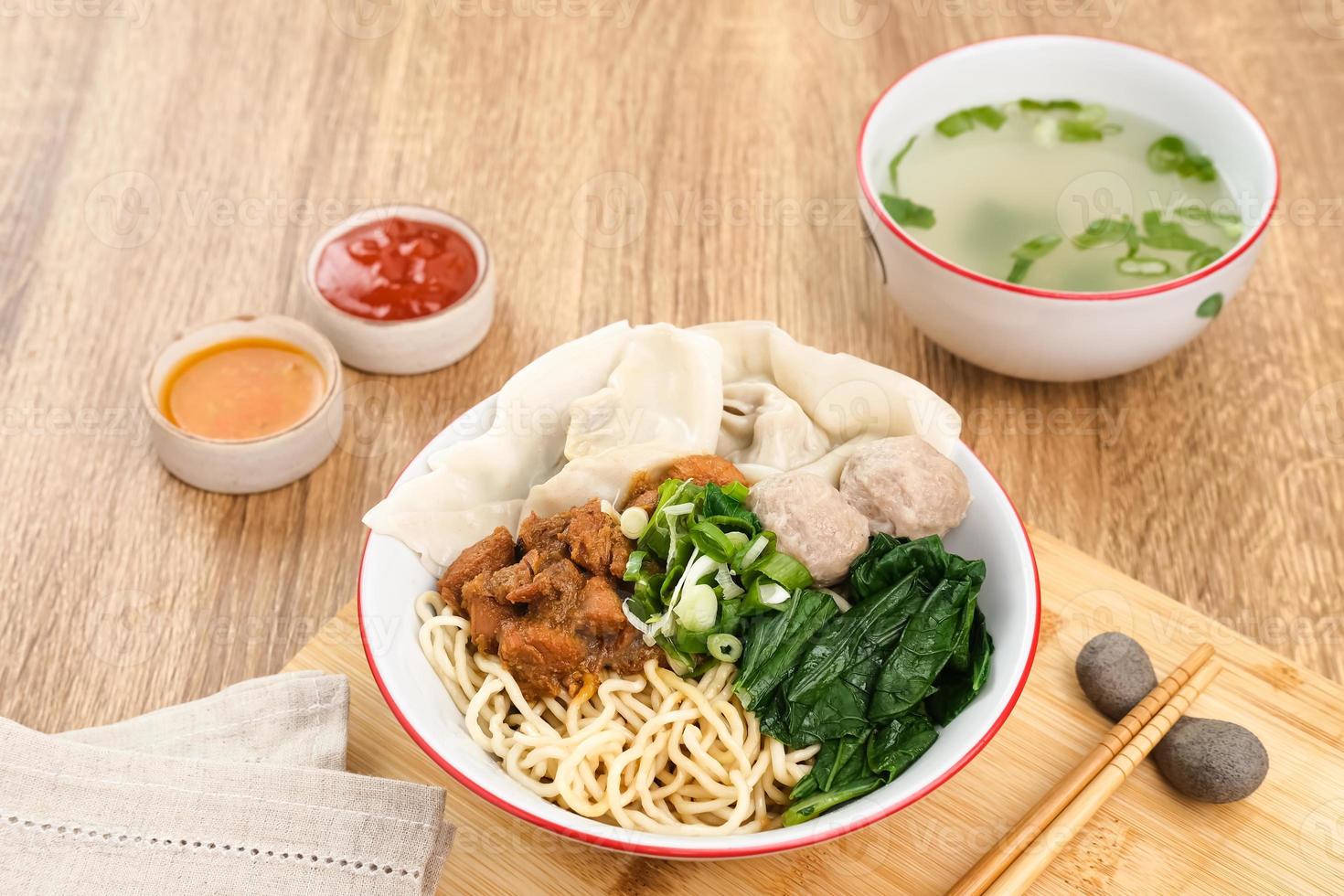 Mie ayam, noodles with chicken, meatballs, dumplings and vegetables, is a popular street food in Indonesia. Served in bowl on wooden table photo