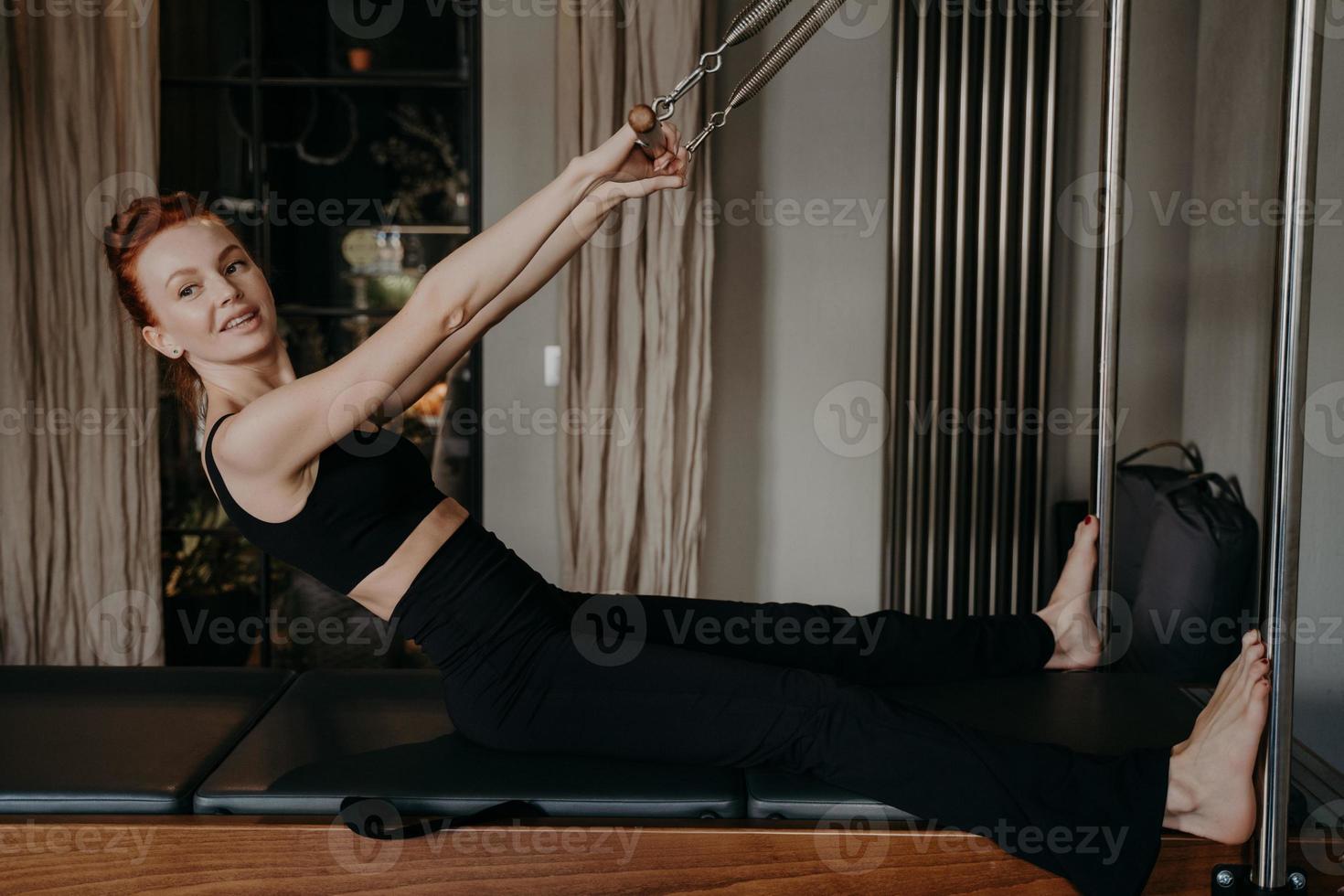 Hermosa joven mujer con sonrisa haciendo ejercicios de reformador de pilates foto