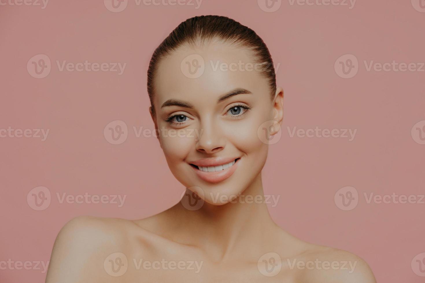 Shirtless beautiful young female model with makeup and clean fresh skin, cares about complexion, smiles gently and looks directly at camera, isolated. Cosmetology, spa, facial treatment concept photo