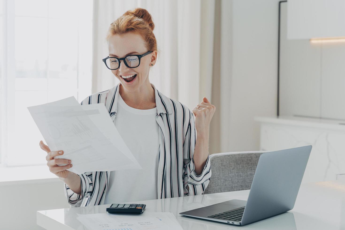 Emotional happy young ginger woman holding paper with last mortgage payment banking notification photo