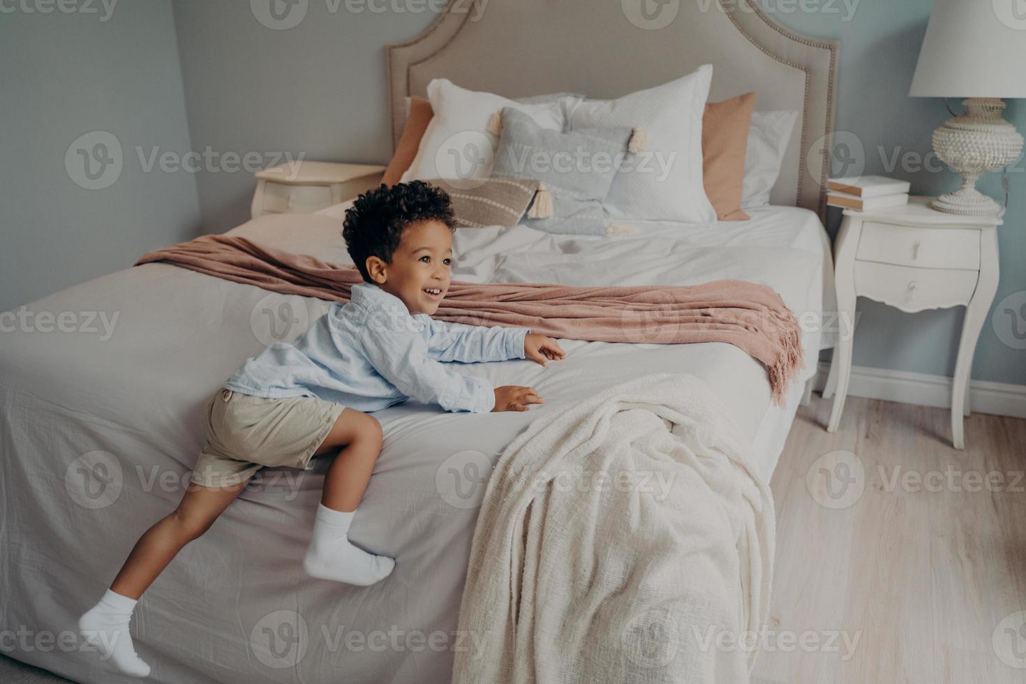 Joyous little african american kid enjoying playtime indoors on bed photo