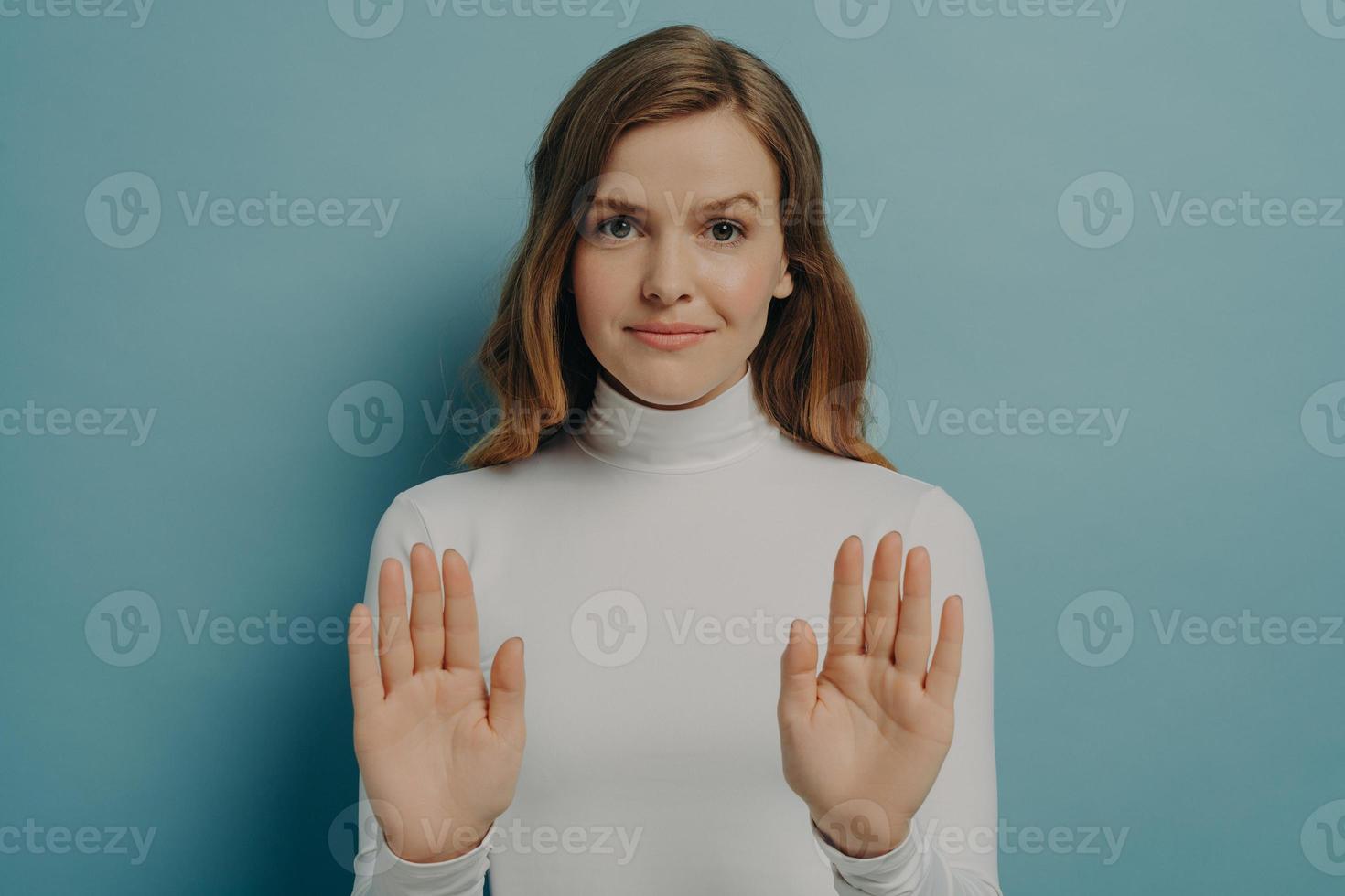 Attractive young focused woman showing stop gesture, saying no, isolated over blue studio background photo