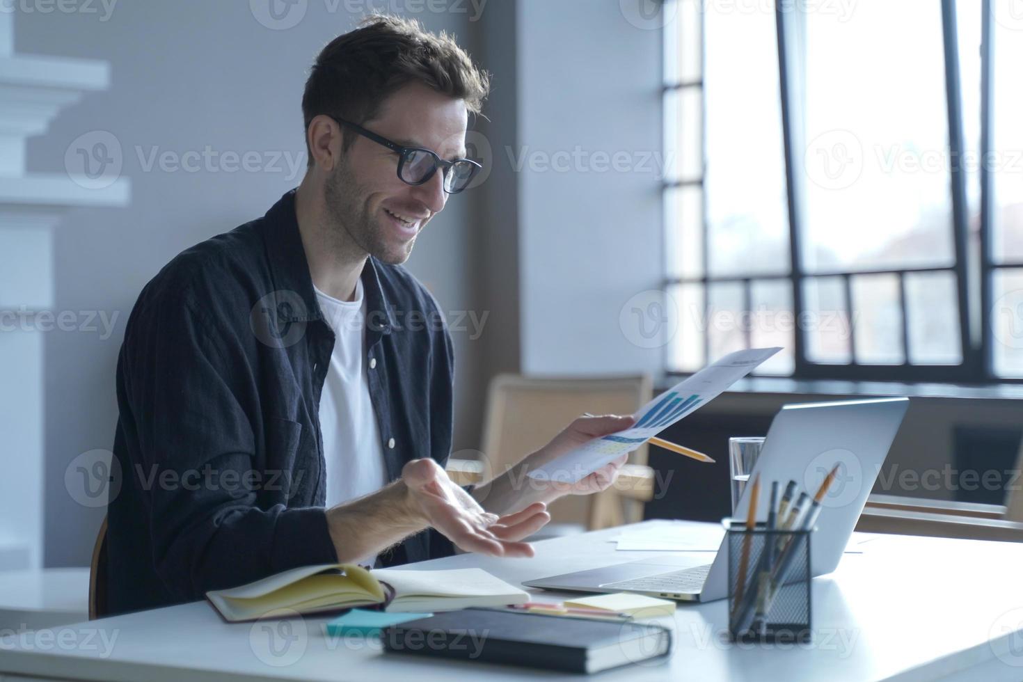 Young German businessman in glasses discussing calculation chart reports with partners online photo
