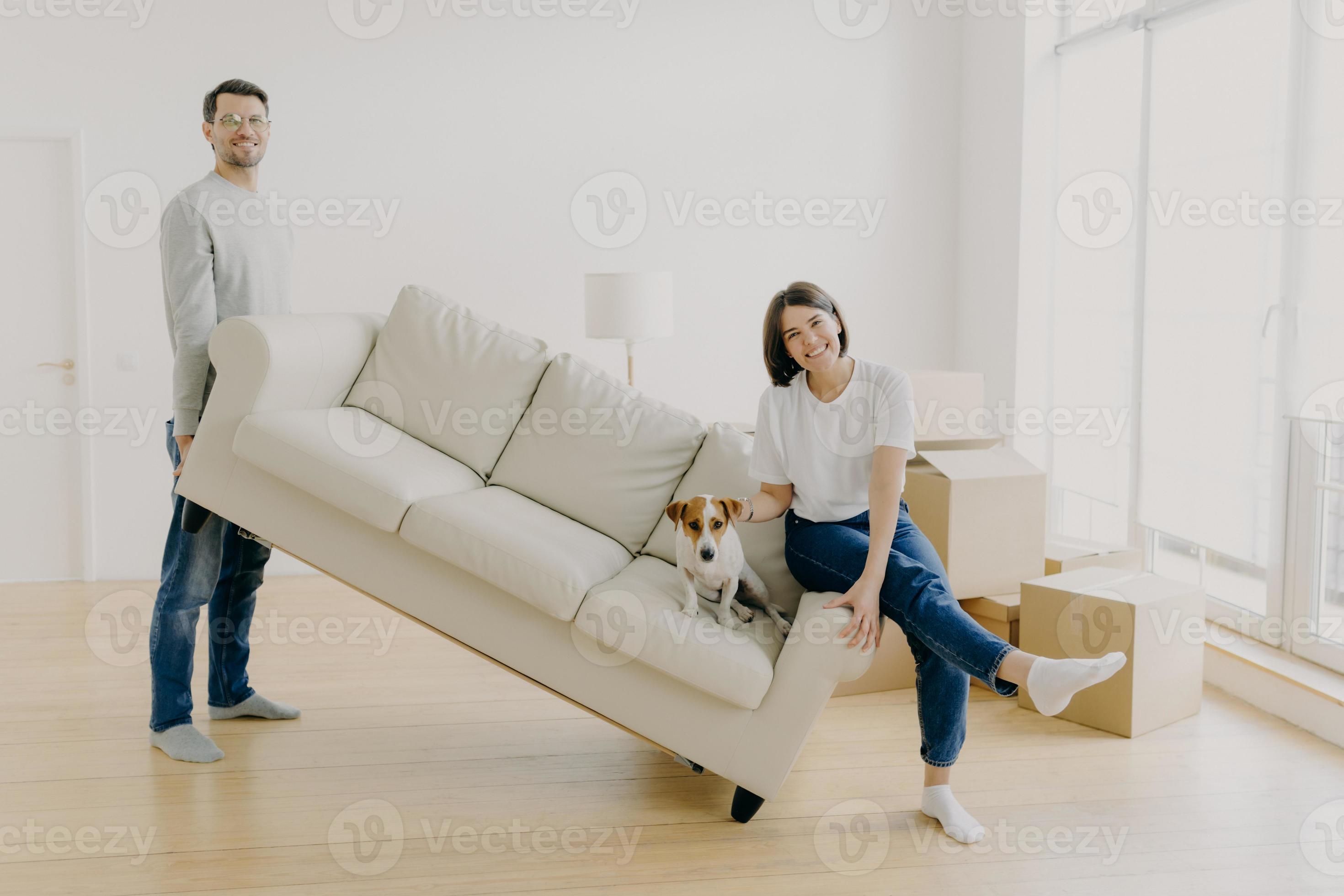 Happy couple move furniture in their new modern home, carry sofa with