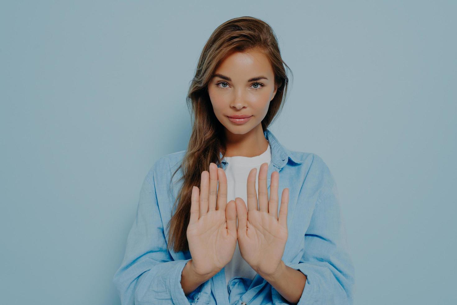 Serious woman showing stop gesture on light blue background photo