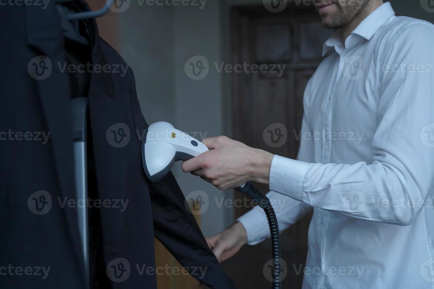 Businessman preparing clothes for meeting with partner, steaming suit with portable steamer photo