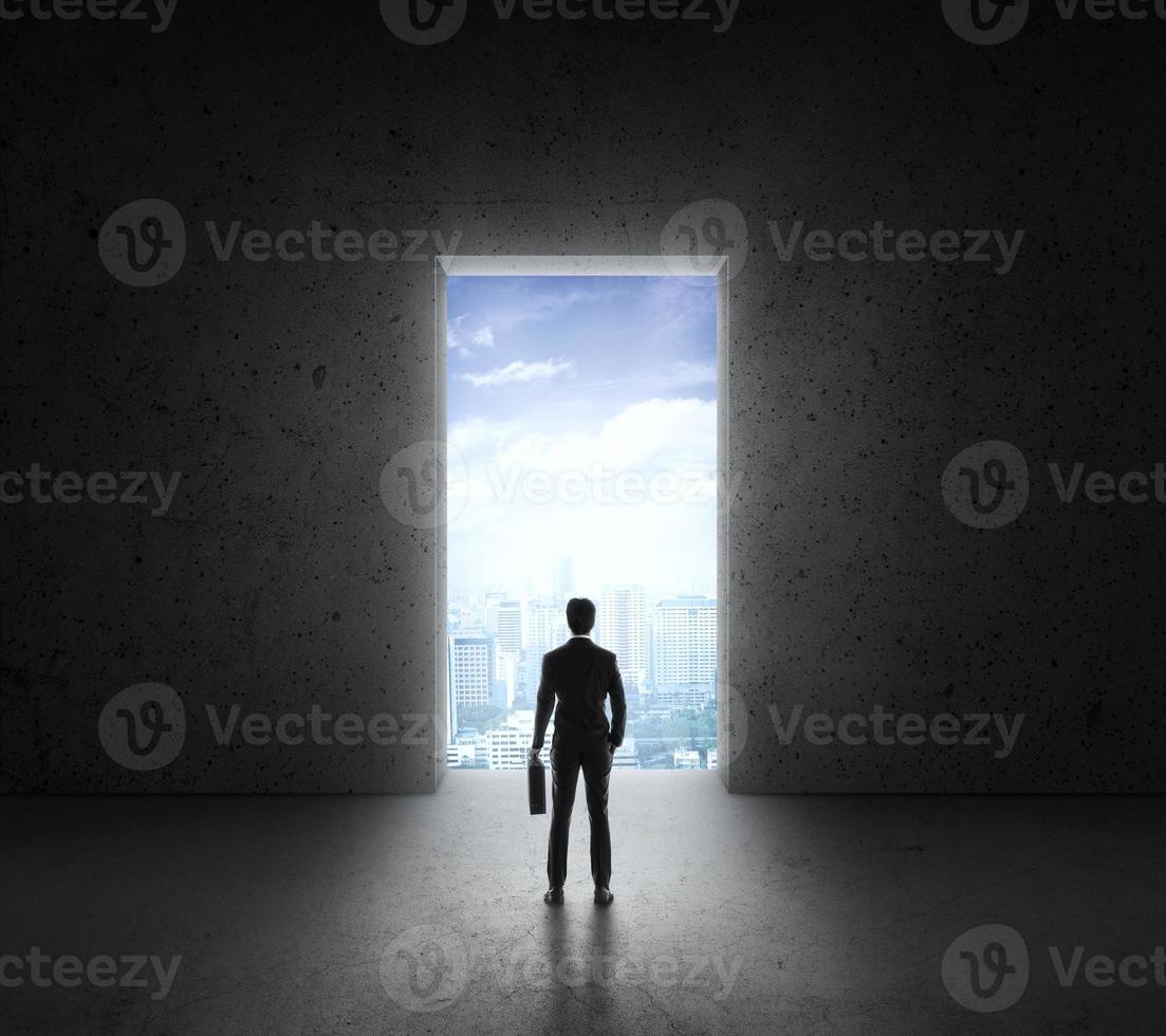 Businessman standing in front of bright big shining door in a concrete wall with a view to the city photo