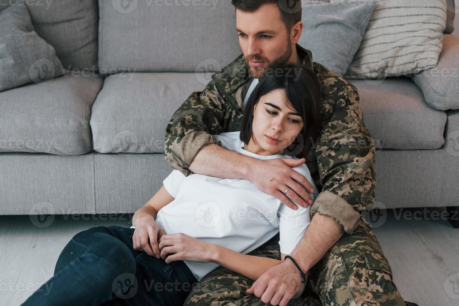 Sitting on the floor and ebracing the woman. Soldier in uniform is at home with his wife photo