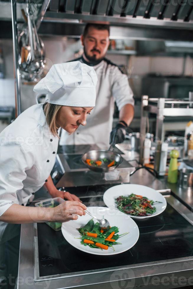 Man and woman working together on the salad. Professional chef preparing food in the kitchen photo