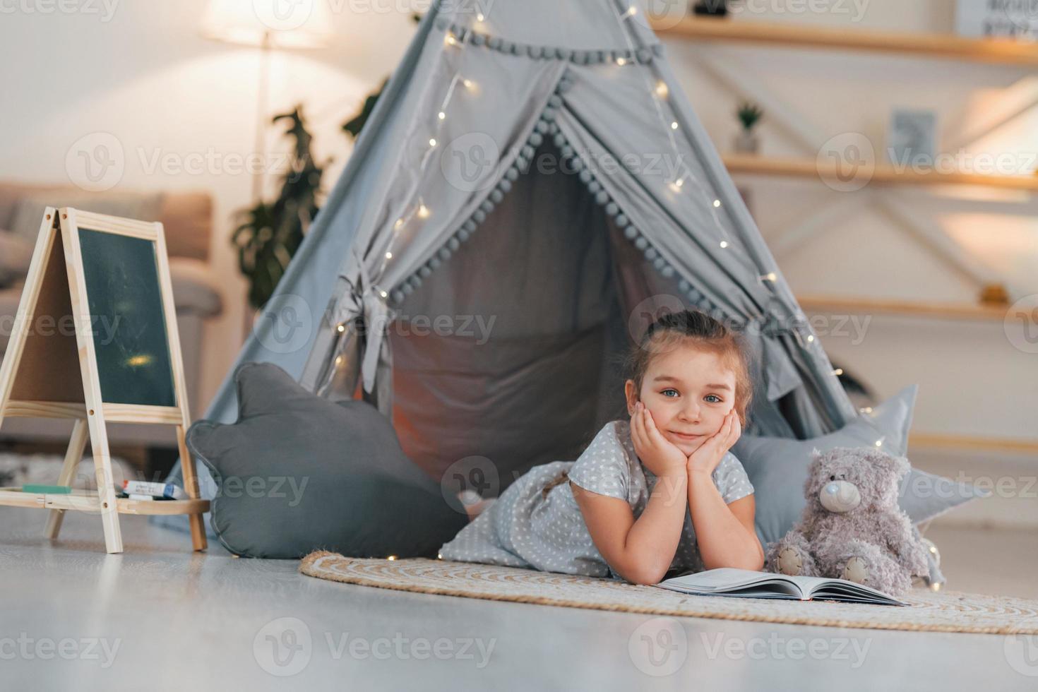 Laying down on the ground. Cute little girl playing in the tent that is in the domestic room photo