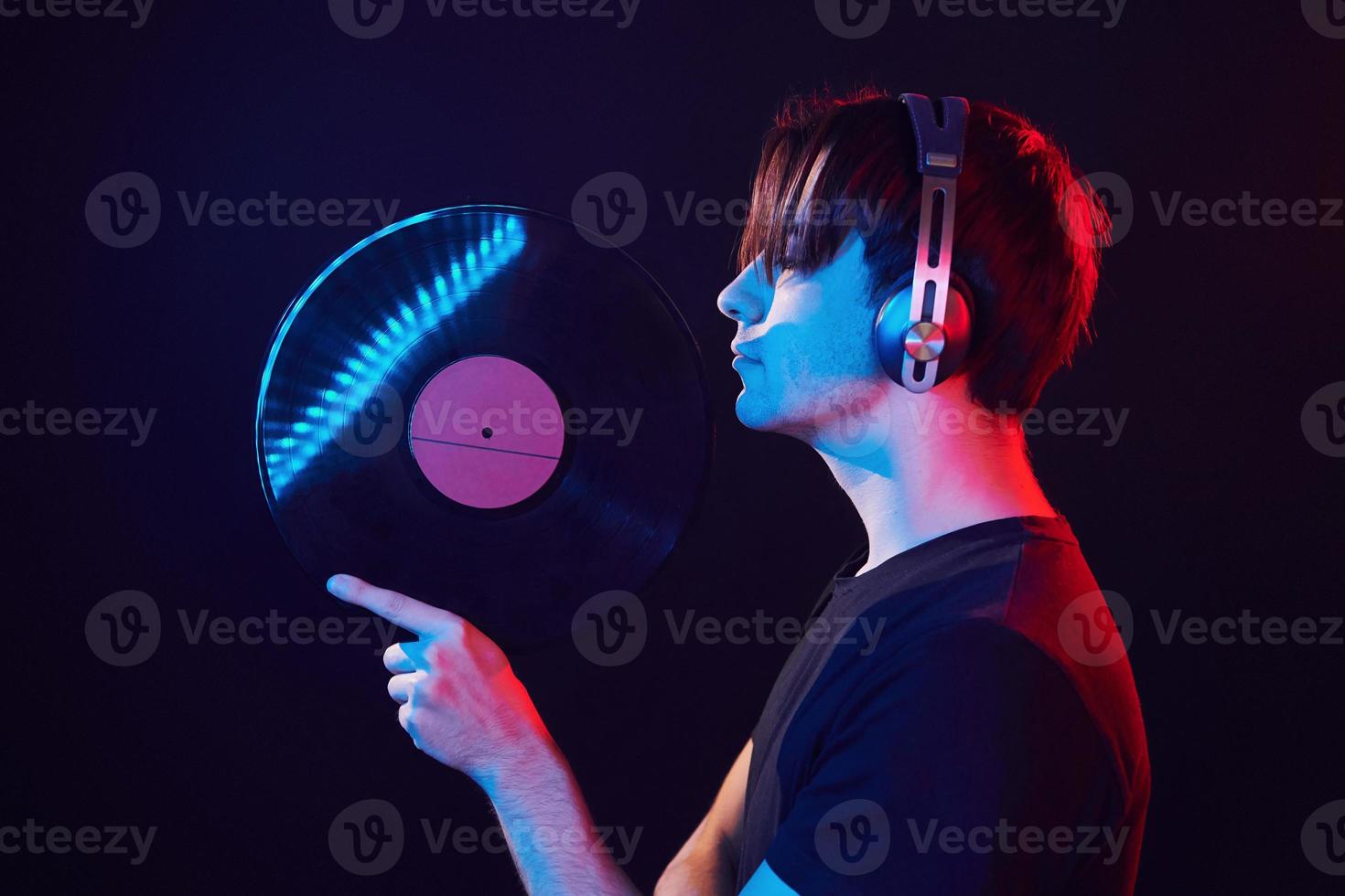 con disco de vinilo en las manos. hombre de pie en el estudio con luz de neón foto