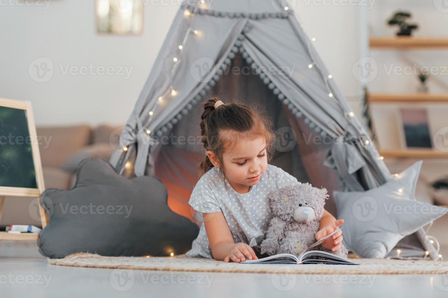Laying down on the ground. Cute little girl playing in the tent that is in the domestic room photo