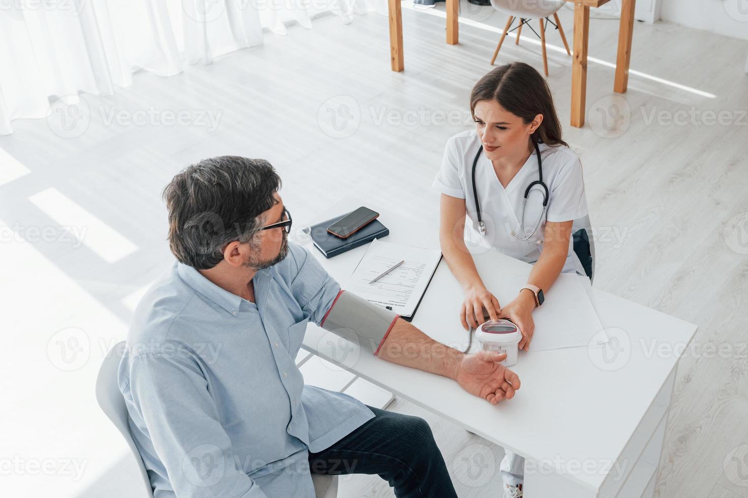 Mature man is with female doctor, having consultation. Professional medical worker in white coat is in the office photo