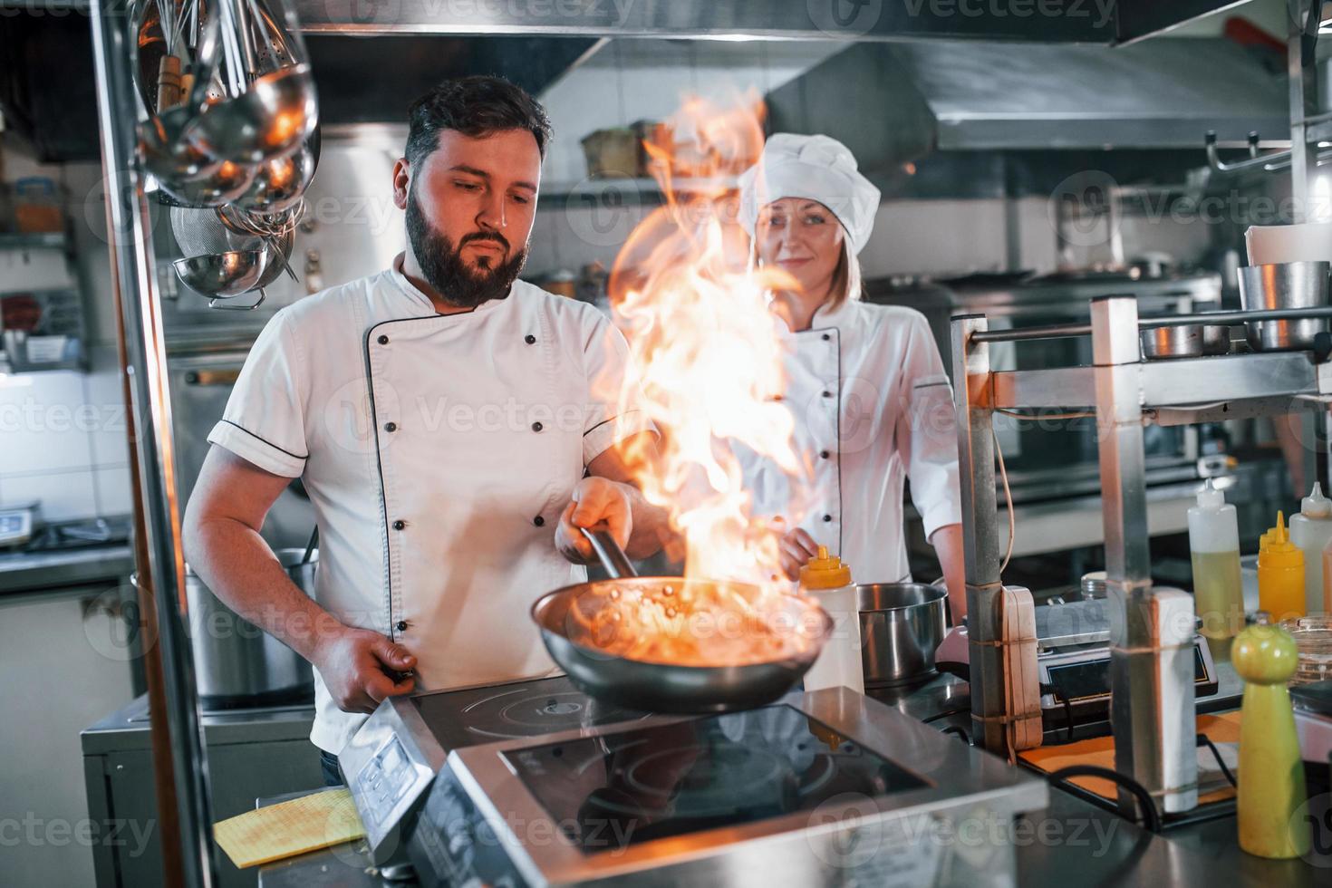 prender fuego a la comida en la sartén. chef profesional preparando comida en la cocina foto