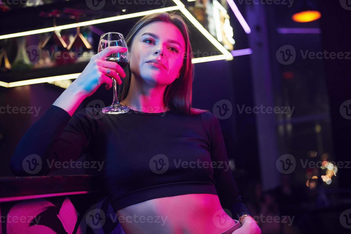 Young woman standing in the night club with drink in hand photo