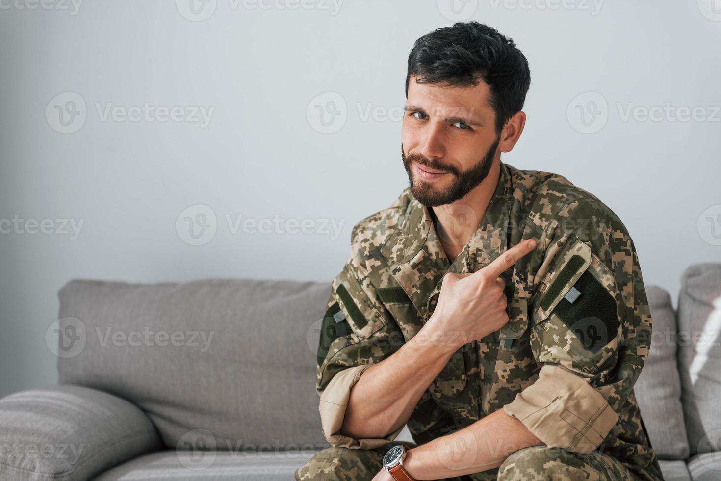 Soldier in uniform is indoors in the domestic room. Sitting on the sofa photo