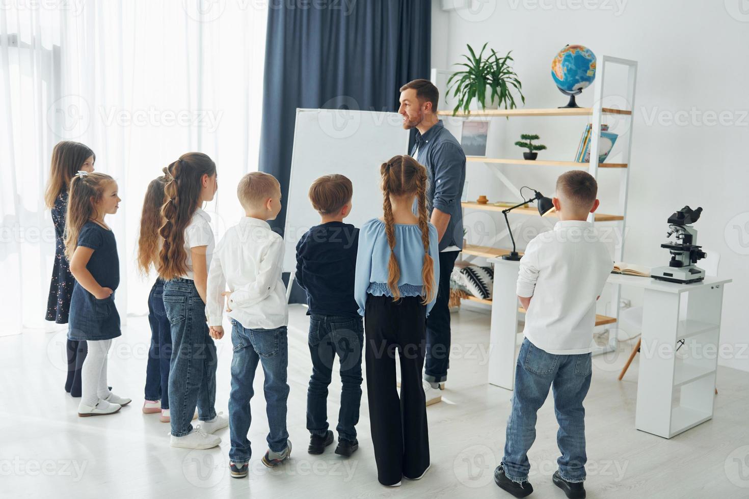 Explaining lesson and using board. Group of children students in class at school with teacher photo