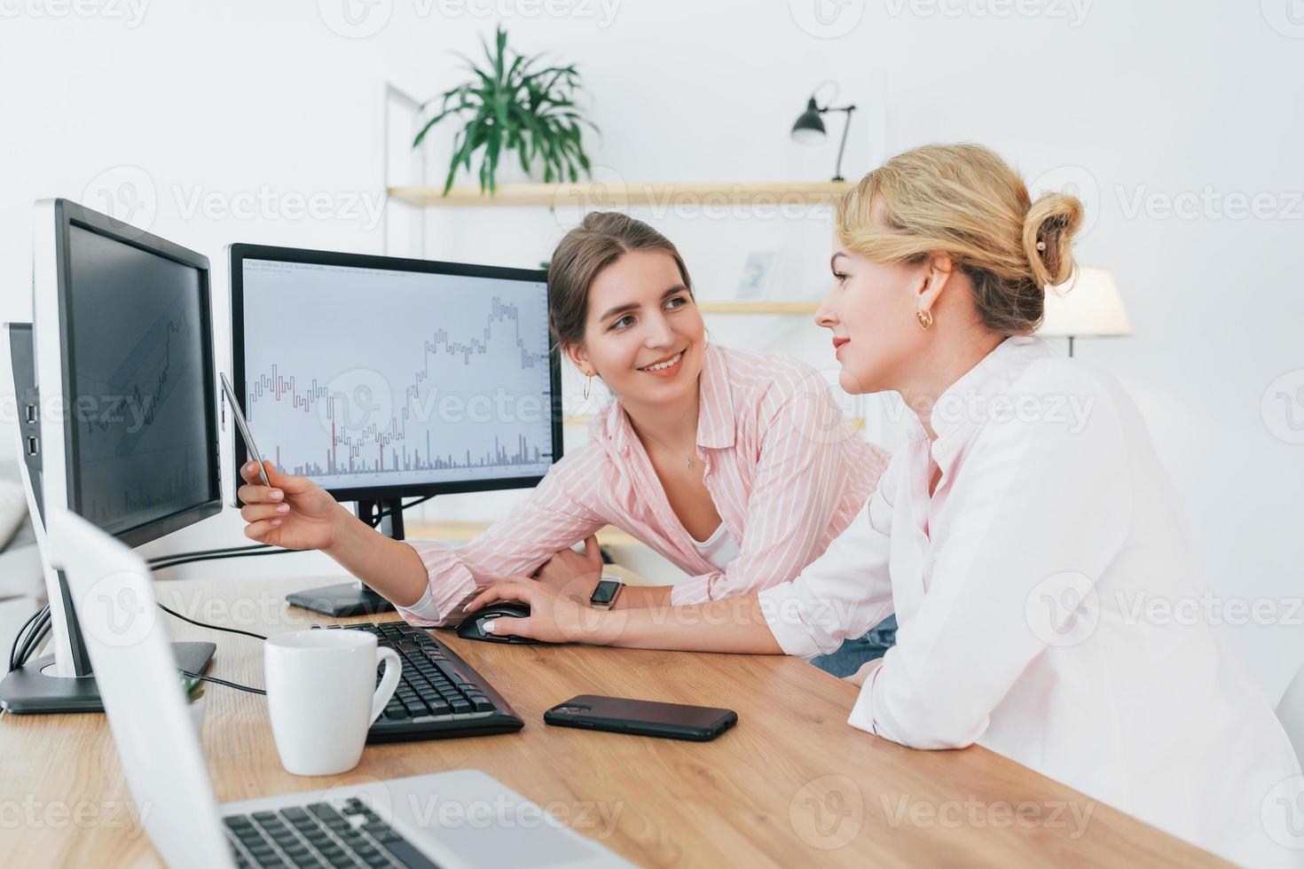 Two female stock brokers in formal wear is working in the office by pc photo