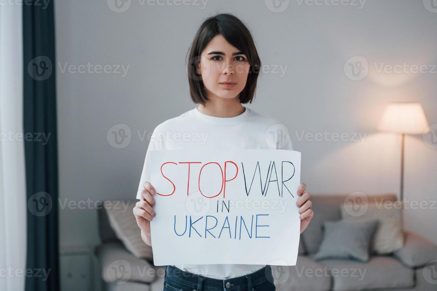 Woman standing at home with poster of stop war in Ukraine photo