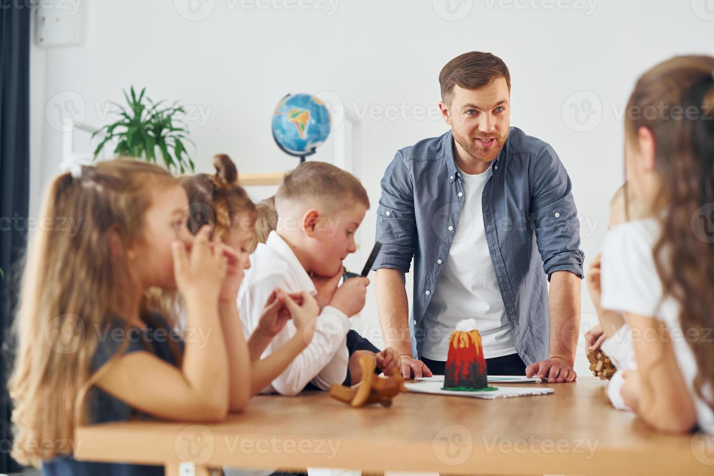pequeño modelo de volcán está sobre la mesa. grupo de niños estudiantes en clase en la escuela con el maestro foto