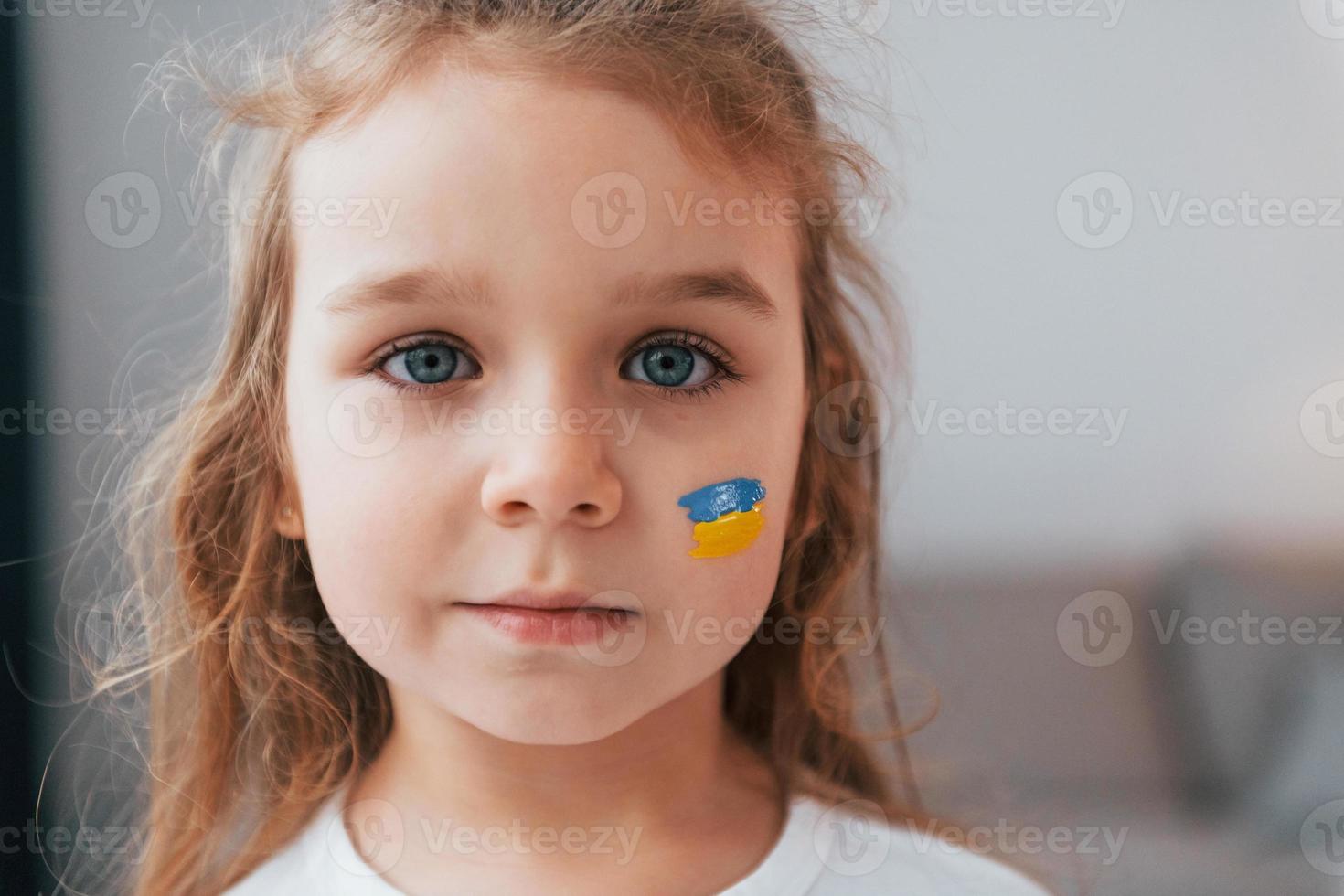 Close up view. Portrait of little girl with Ukrainian flag make up on the face photo
