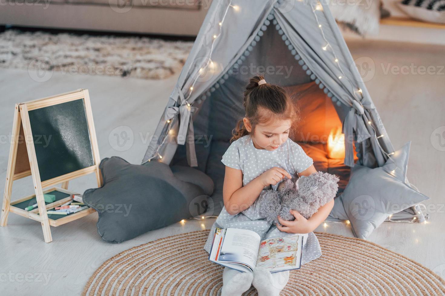 At daytime. Cute little girl playing in the tent that is in the domestic room photo